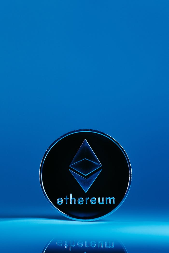A vertical shot of an Ethereum coin standing on a reflective surface with a blue background.