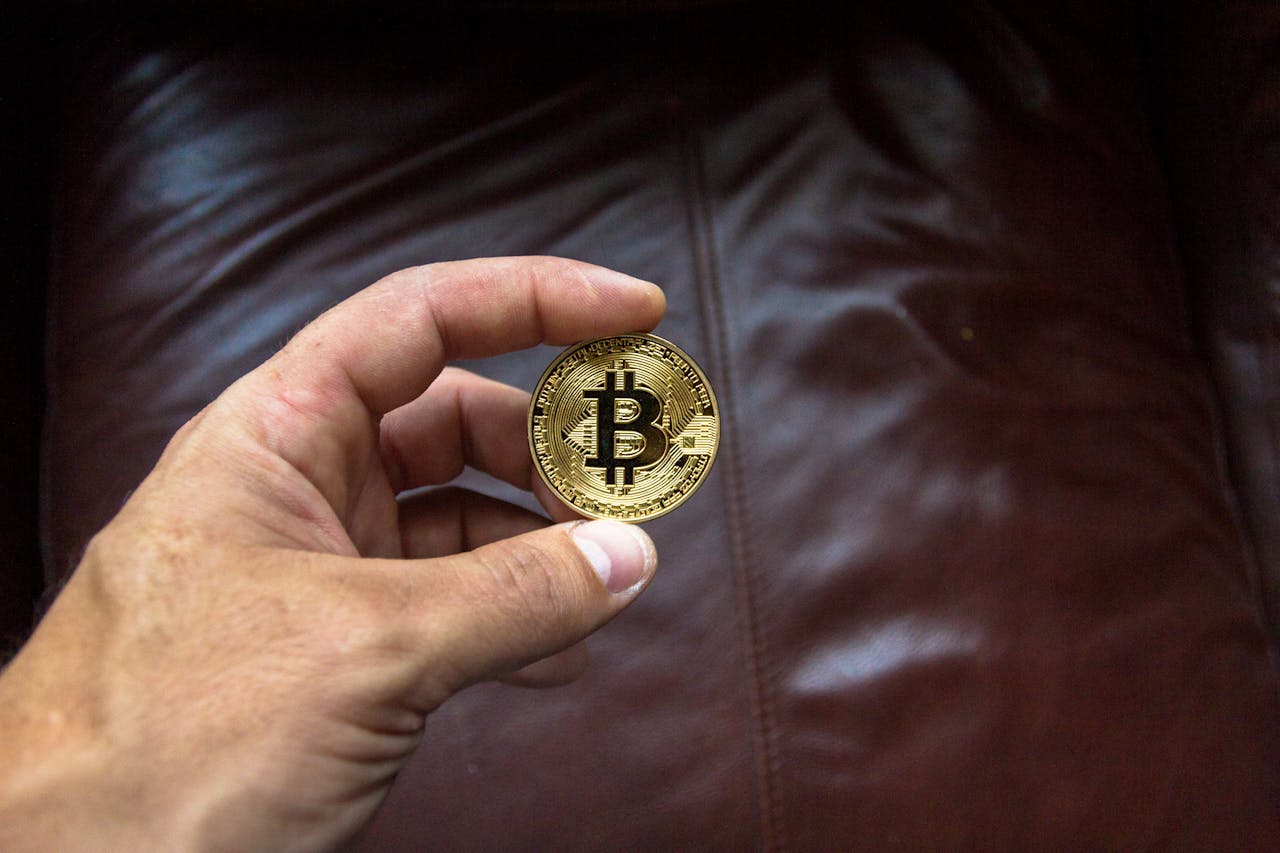 about-01 Close-up of a hand holding a gold Bitcoin cryptocurrency coin on a leather background.